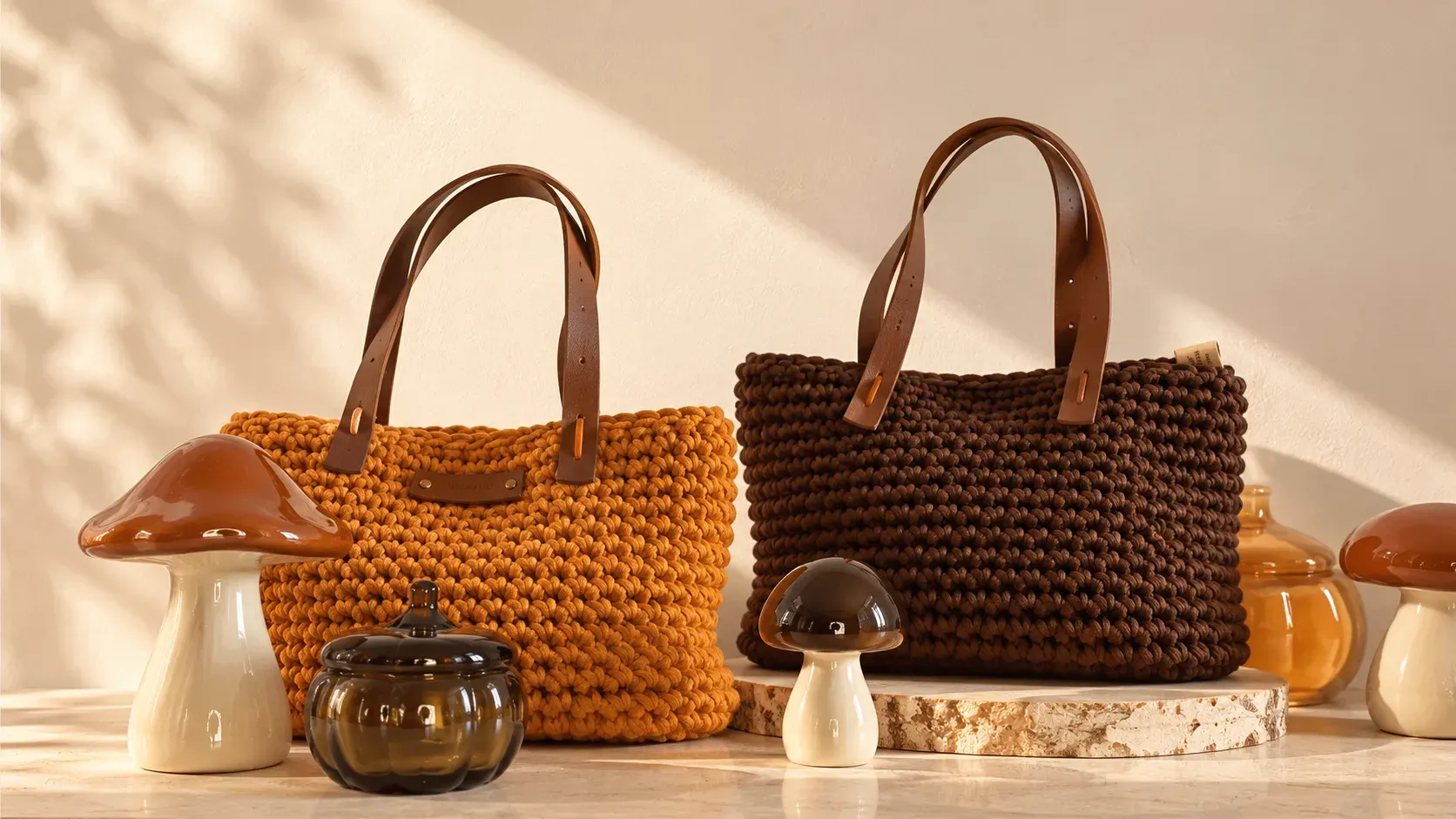 Deux sacs en crochet, orange et chocolat, à anses en cuir, posés dans une lumière dorée parmi des champignons en céramique