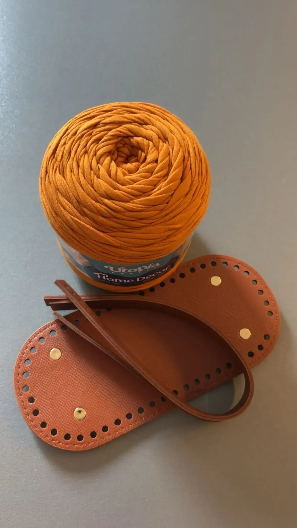 Une pelote de fil orange, un fond de sac en cuir et des anses en cuir, avant l’assemblage