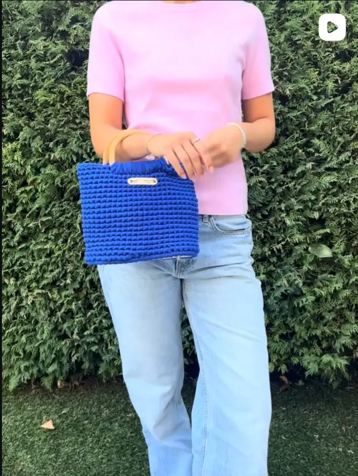 Sac en crochet bleu tenu à la main, devant une haie