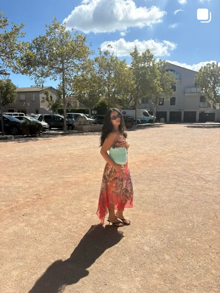 Silhouette en robe d’été sur une place ensoleillée, sac à l’épaule