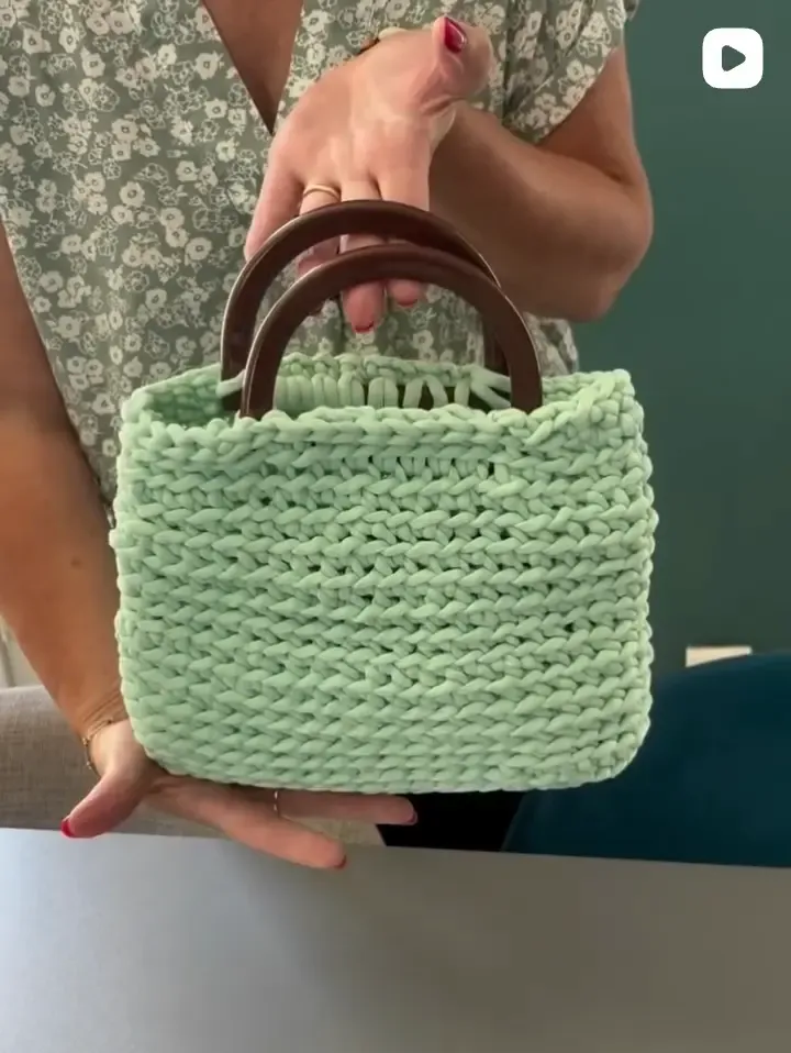 Sac en crochet vert d’eau à anses rigides, tenu à deux mains